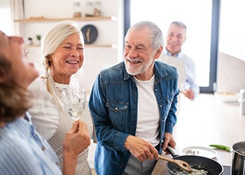 older couple cooking dinner for a group and laughing