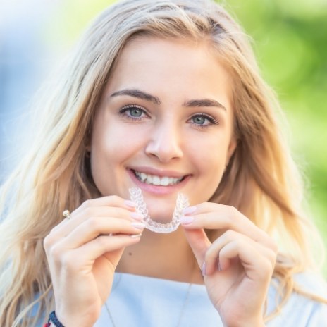 Smiling blonde woman holding a clear aligner