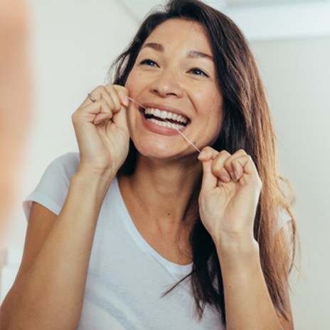 Woman smiling while flossing her teeth at home