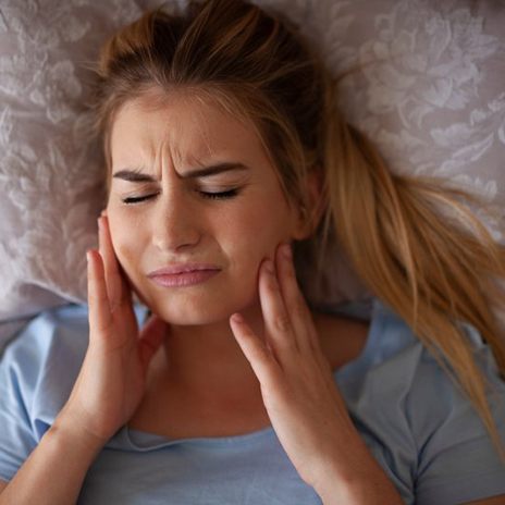 Woman rubbing her jaw while lying down in bed